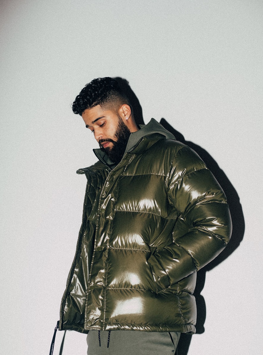 South Asian man in a puffer jacket posing by looking downward.