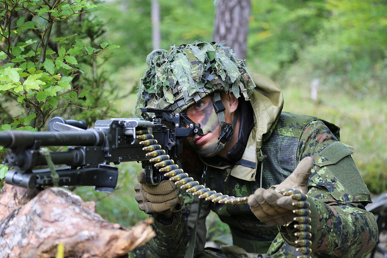 Un soldat canadien vise une mitrailleuse polyvalente C6 tout en tenant une bande de munitions.