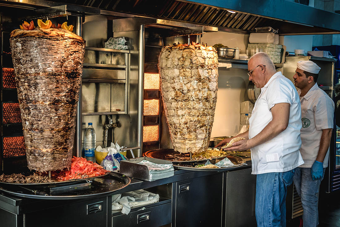 Two batches of shawarma in a kitchen with two cooks